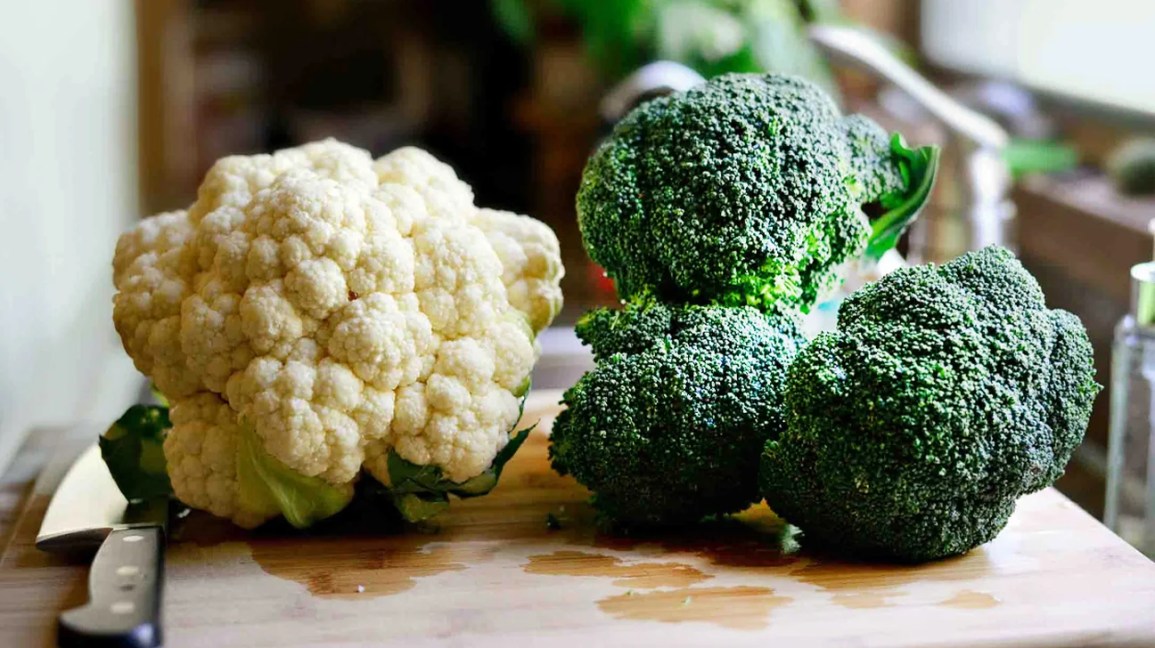 raw heads of cauliflower and broccoli on a cutting board