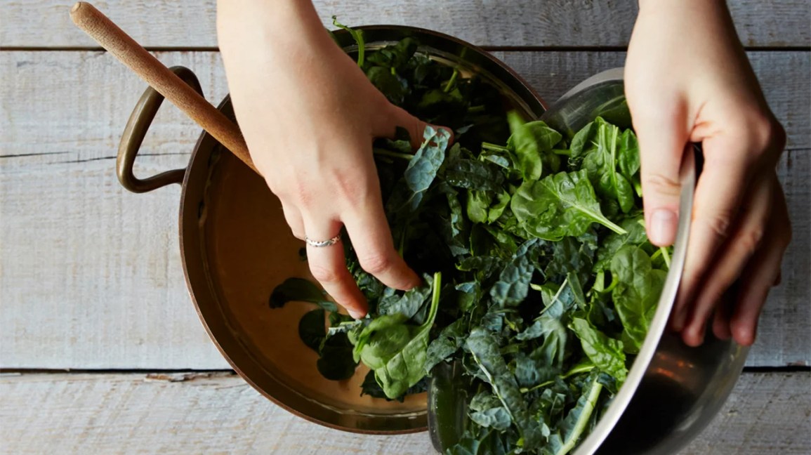 hands scooping raw kale and spinach into a bowl