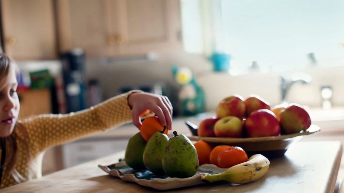Young child reaching for fruit on a platter
